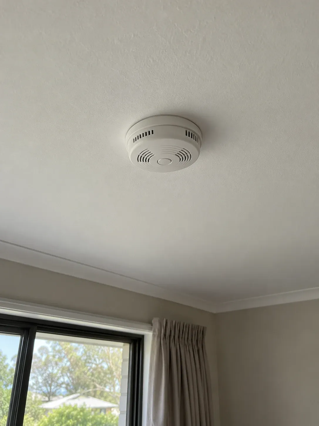 Ceiling-mounted smoke alarm above a bedroom window